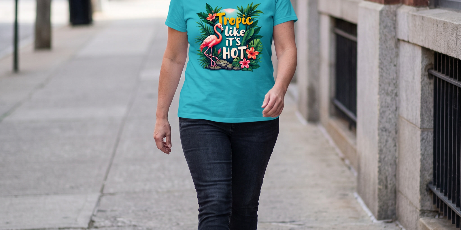 A woman striding down a city sidewalk in the Tropic Like It's Hot flamingo tee