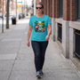 A woman striding down a city sidewalk in the Tropic Like It's Hot flamingo tee