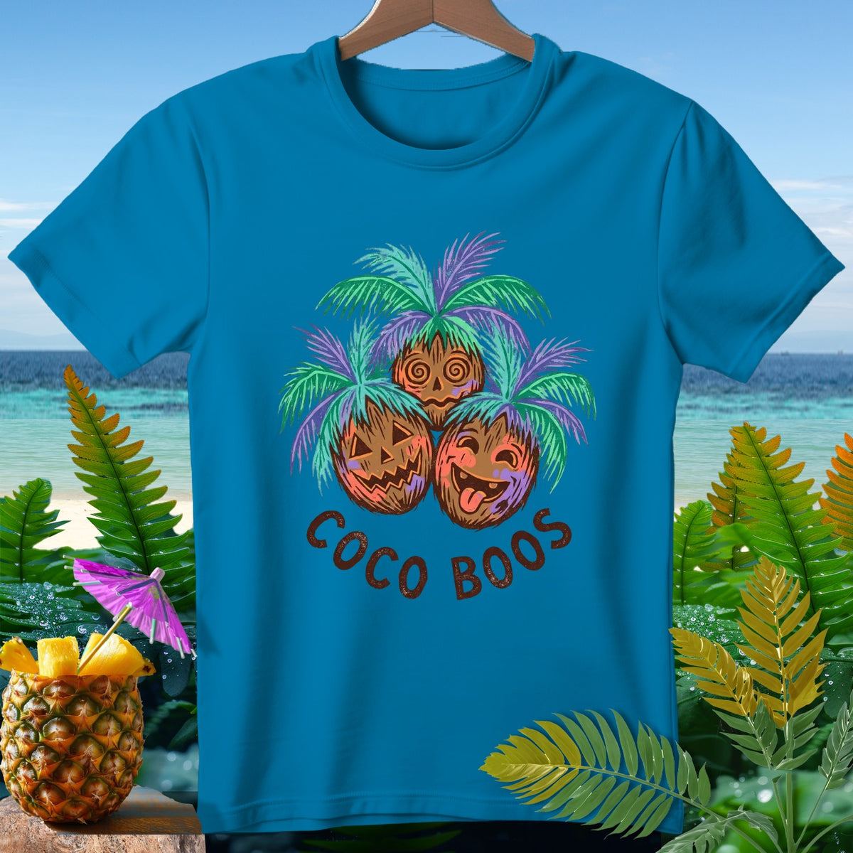 T-shirt with three coconuts as jack-o'-lanterns under palm trees, text "COCO BOOS".