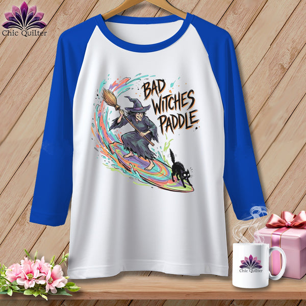 White and blue raglan t-shirt with a witch and black cat graphic that reads "Bad Witches Paddle".
