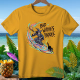 Yellow t-shirt with a witch surfing on a broom and black cat, text 