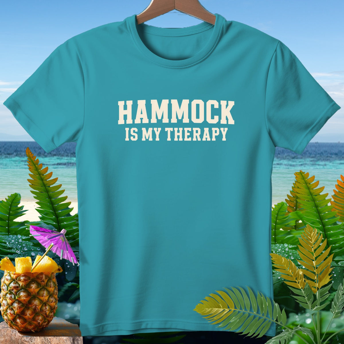 Teal t-shirt with "HAMMOCK IS MY THERAPY" text, beach and tropical plants background.