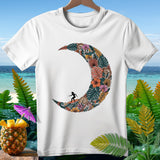 White t-shirt with crescent moon design filled with tropical foliage and a surfer.
