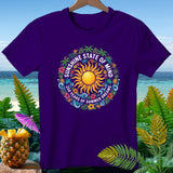 Purple t-shirt with a circular sun, flowers, and 
