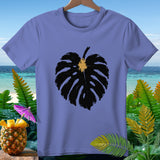 Purple t-shirt with black monstera leaf graphic, set against tropical beach and pineapple cocktail.