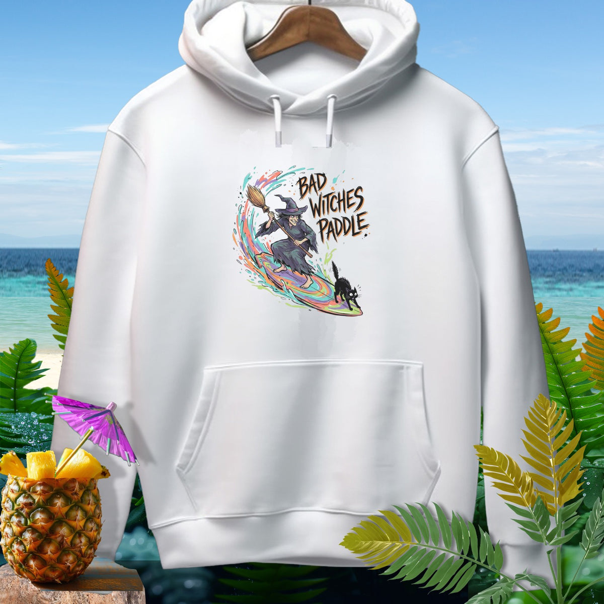 White hoodie with "Bad Witches Paddle" graphic featuring a witch surfing.