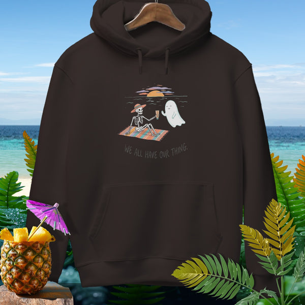 Brown hoodie with graphic of skeleton and ghost on beach, text "WE ALL HAVE OUR THING."