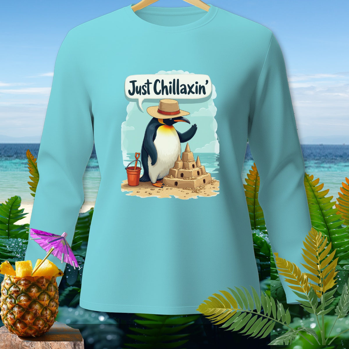 Light blue long-sleeve shirt with a penguin building a sandcastle, saying "Just Chillaxin'".
