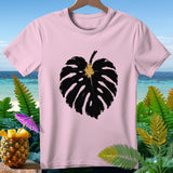 Pink t-shirt with a large black monstera leaf graphic and tropical background.