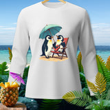 White long-sleeve shirt with cartoon penguins under an umbrella on a beach.