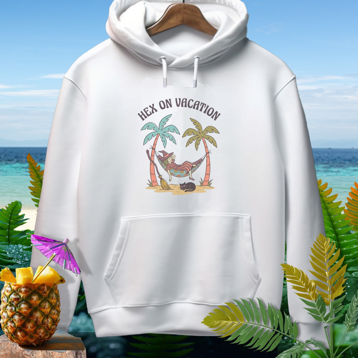 White hoodie with a graphic of a witch relaxing in a hammock that says "Hex on Vacation".