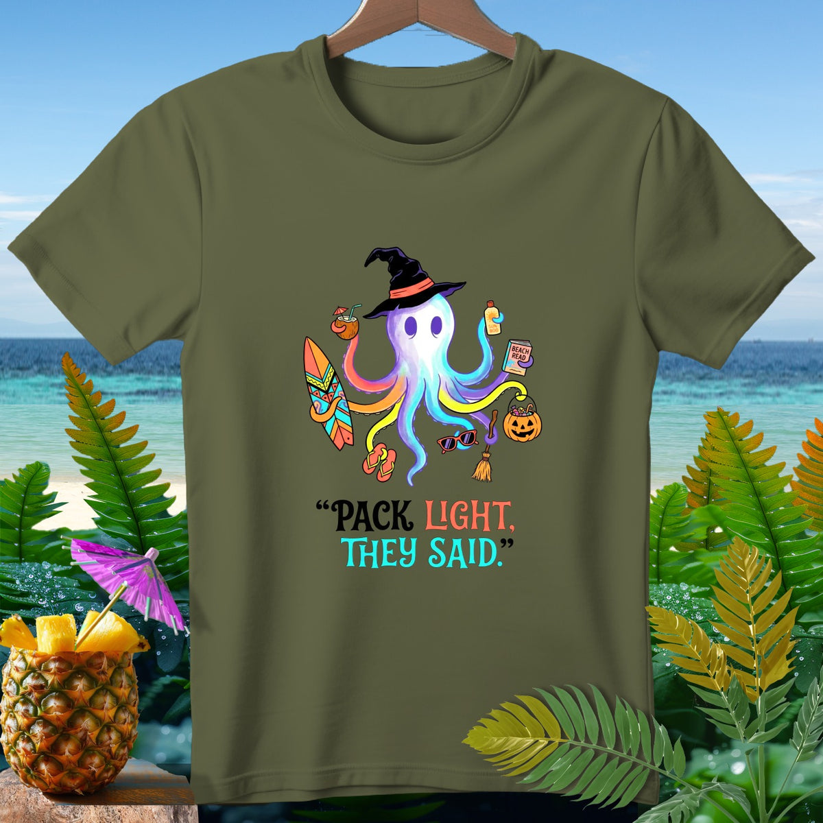 Olive green t-shirt with octopus wearing witch hat and beach items, text "PACK LIGHT, THEY SAID."