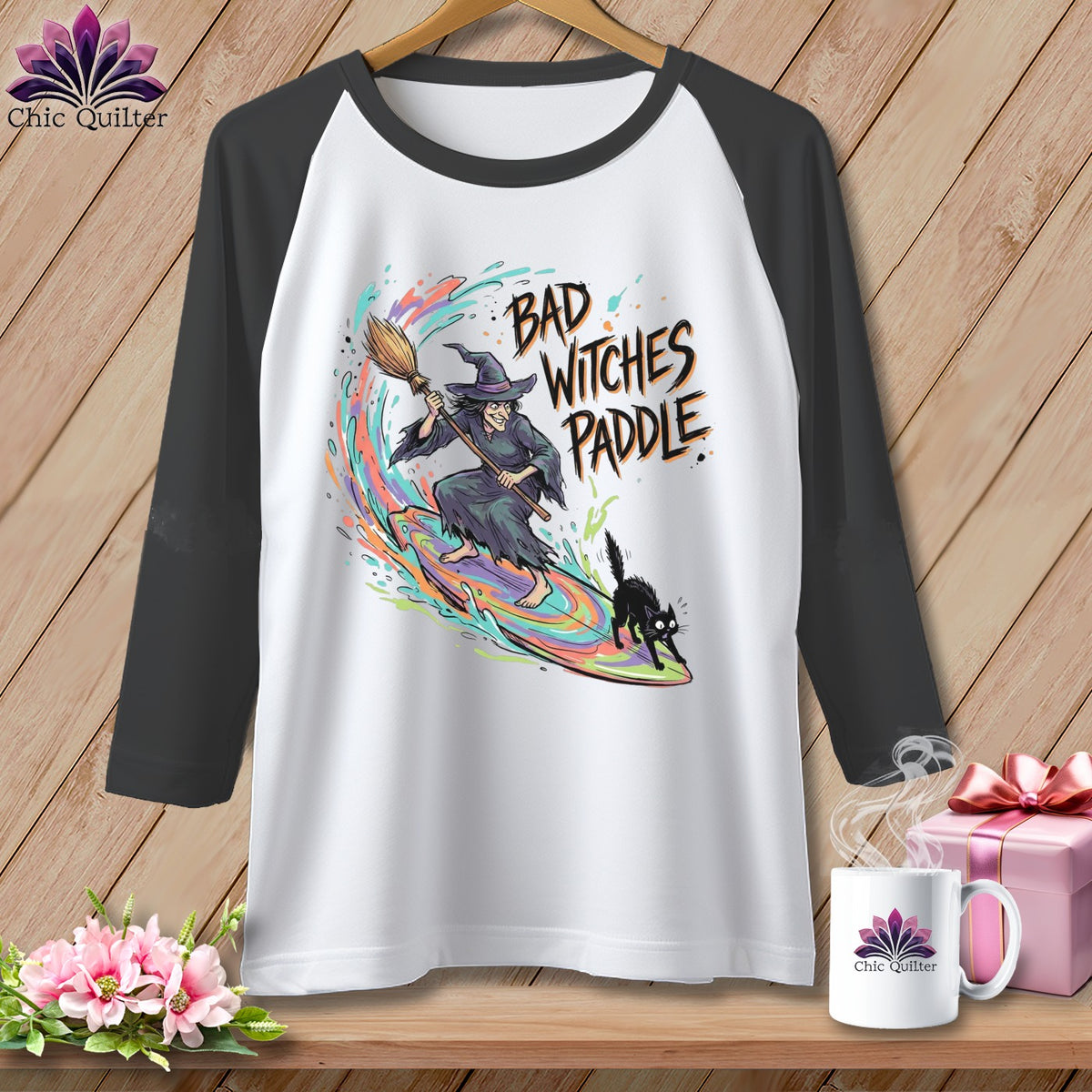 Witch surfing on colorful wave with black cat and "Bad Witches Paddle" text.