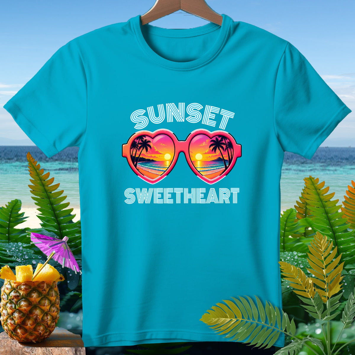 Blue t-shirt with "Sunset Sweetheart" text and heart-shaped sunglasses with sunset scene.