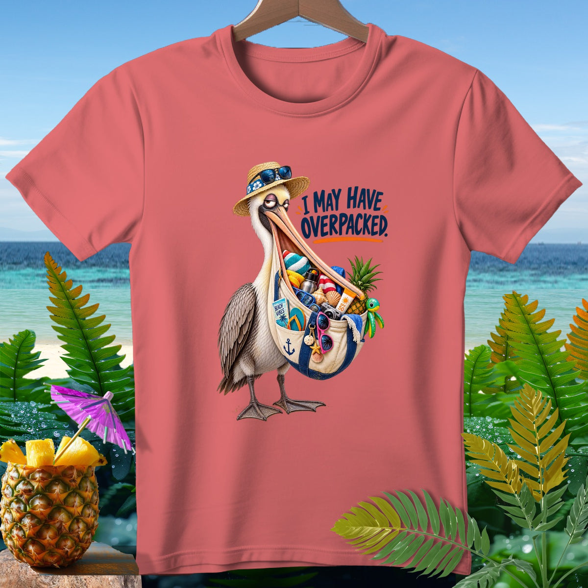 Pelican wearing a straw hat and sunglasses spills beach items from a bag, text "I MAY HAVE OVERPACKED".
