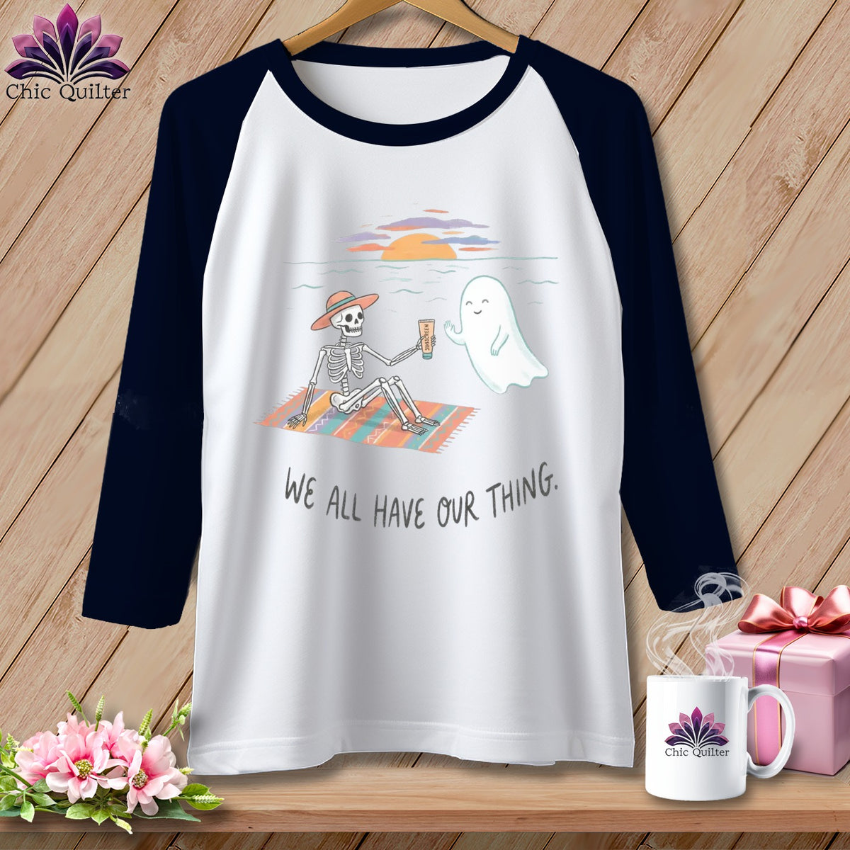 Skeleton and ghost enjoying a beach sunset with "WE ALL HAVE OUR THING." text.