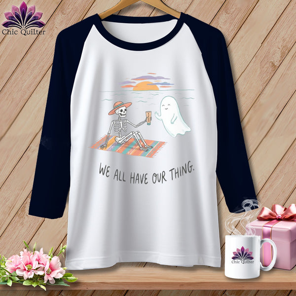 Skeleton and ghost enjoying a beach sunset with "WE ALL HAVE OUR THING." text.