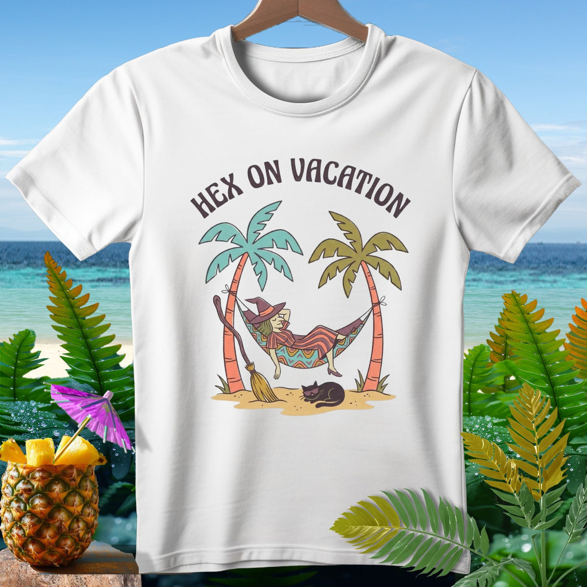 White t-shirt with a witch relaxing in a hammock on a beach, with text "Hex on Vacation".