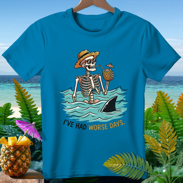 Skeleton in ocean with shark fin, holding pineapple drink, text "I'VE HAD WORSE DAYS."