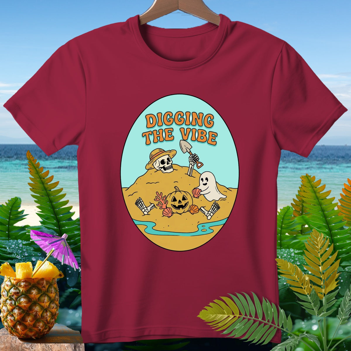 Burgundy t-shirt with a graphic of a skeleton, ghost, and pumpkin digging.