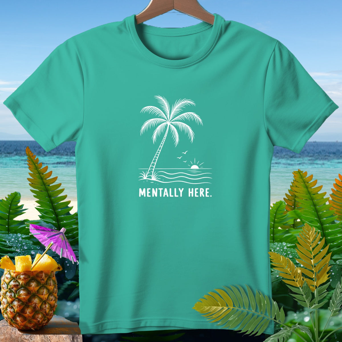 Teal t-shirt with white graphic of palm tree, waves, sun, birds, and text "MENTALLY HERE."