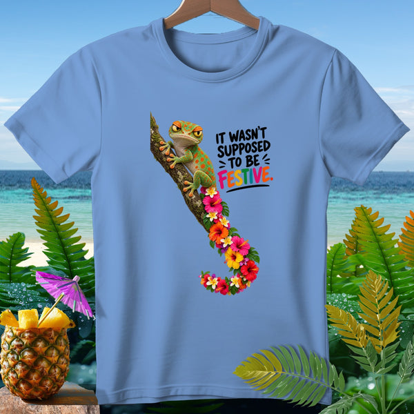 Light blue t-shirt with a green gecko on a branch, surrounded by flowers, and text that reads "IT WASN'T SUPPOSED TO BE FESTIVE."