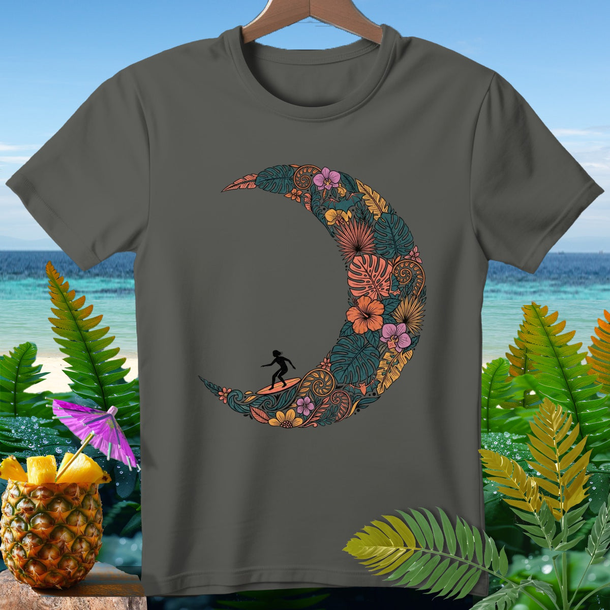 Dark gray t-shirt featuring a crescent moon design filled with tropical foliage and flowers, with a surfer silhouette.
