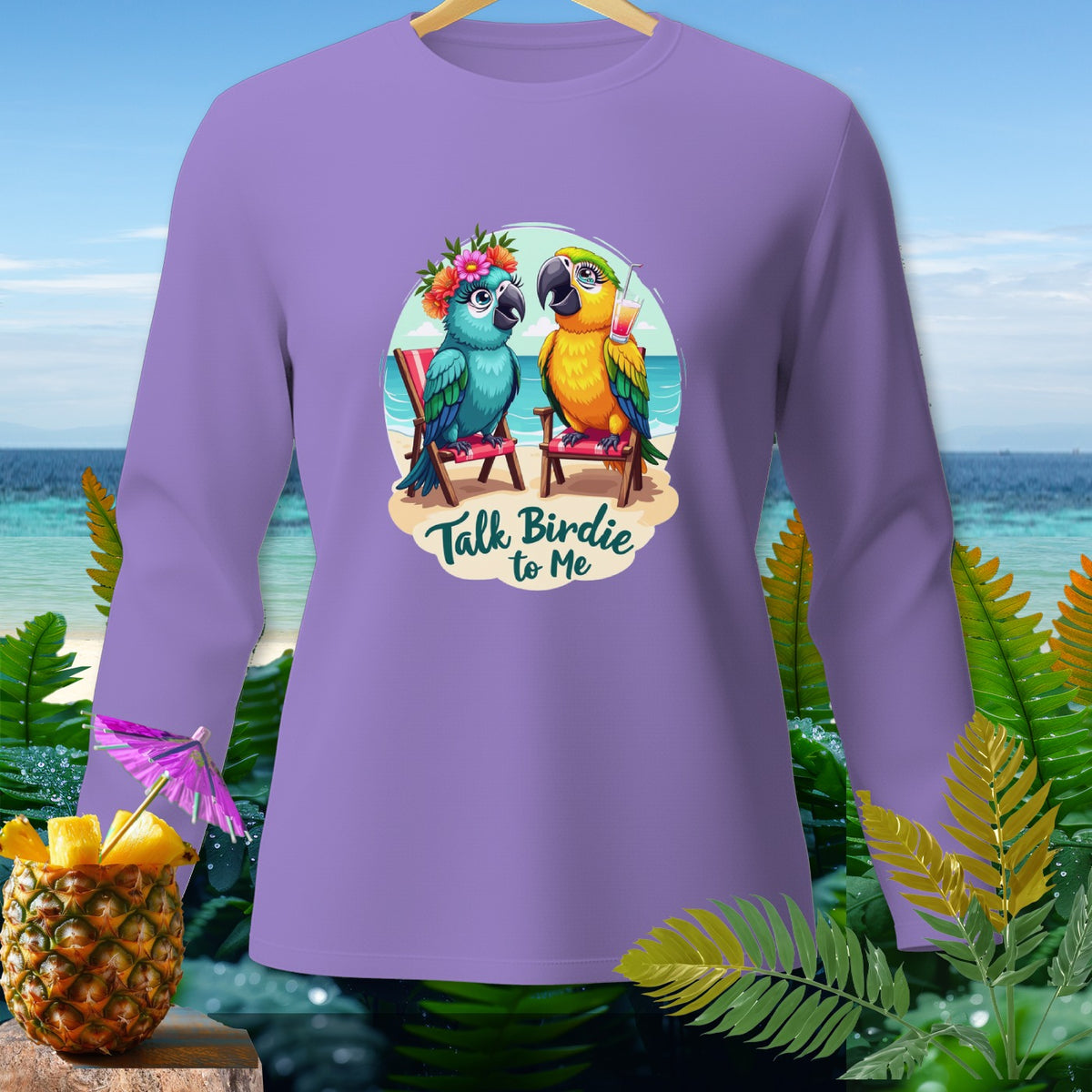 Long-sleeve lilac t-shirt with cartoon parrots on beach chairs and "Talk Birdie to Me" text.