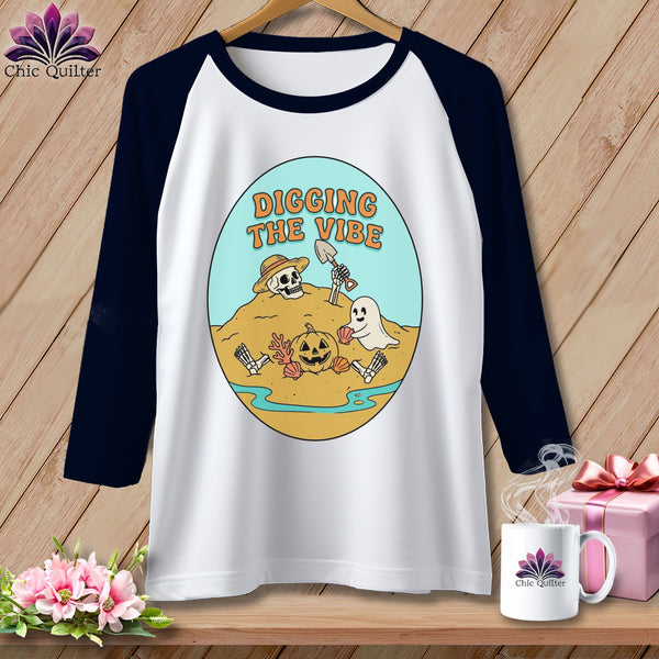 White baseball tee with Halloween graphic of skeleton, ghost, pumpkin, and text "Digging the Vibe".