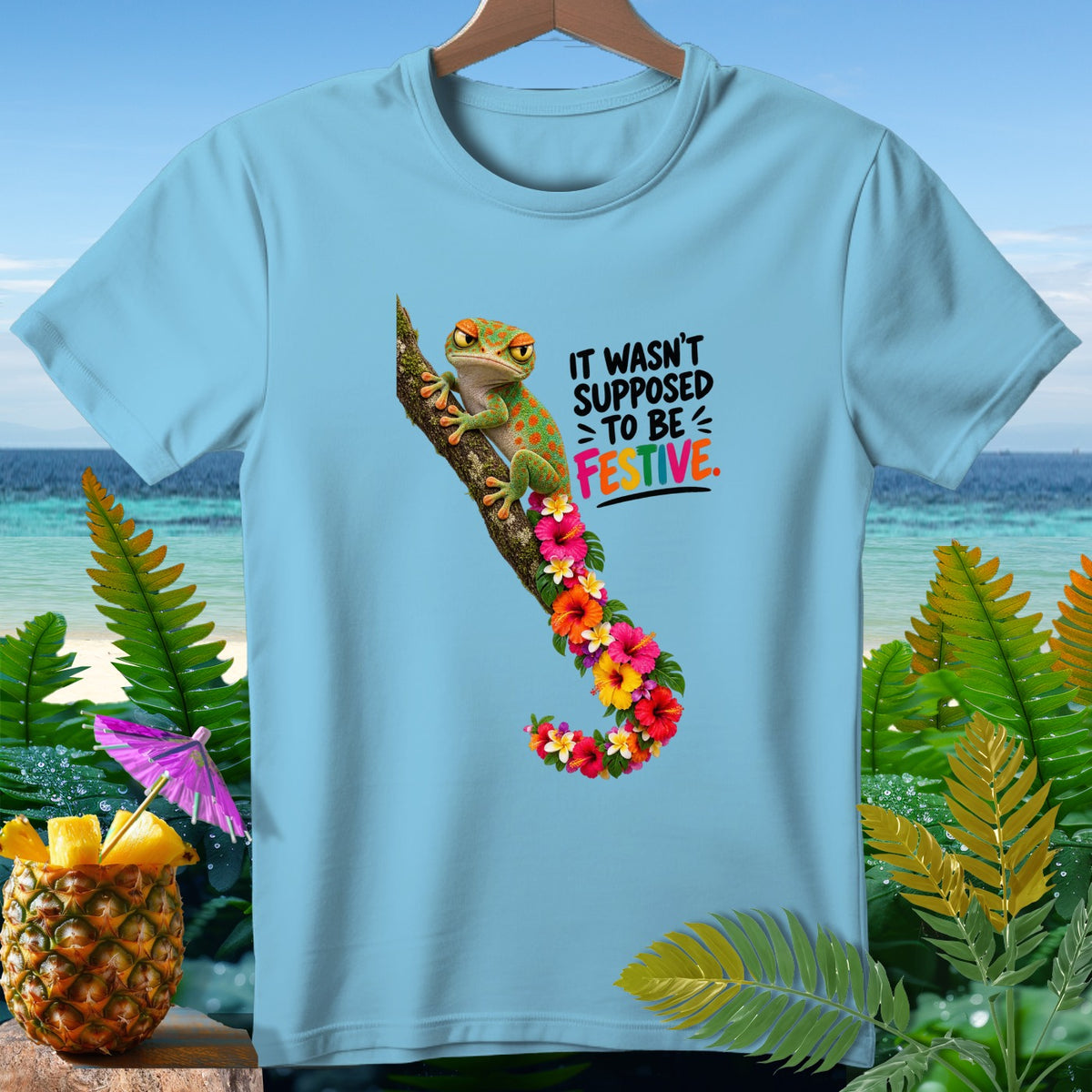 Light blue t-shirt with a gecko on a branch surrounded by flowers and the text "IT WASN'T SUPPOSED TO BE FESTIVE."