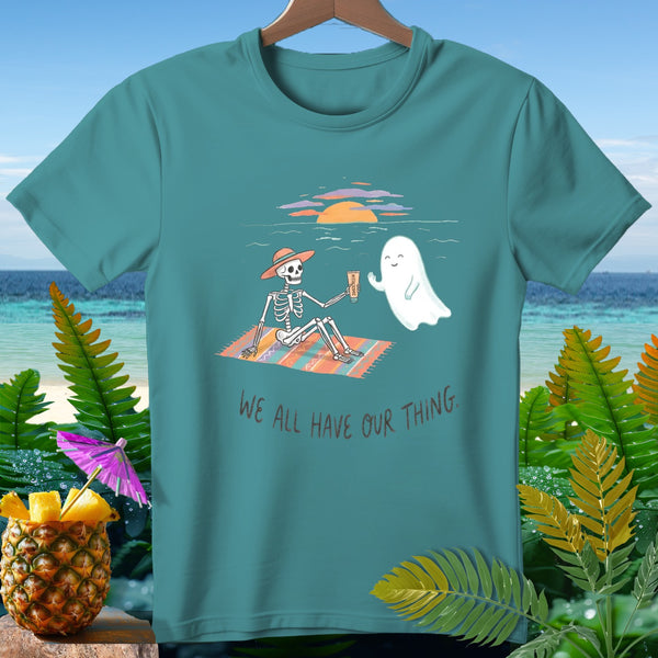 Skeleton with a ghost on a beach blanket, with text "WE ALL HAVE OUR THING."