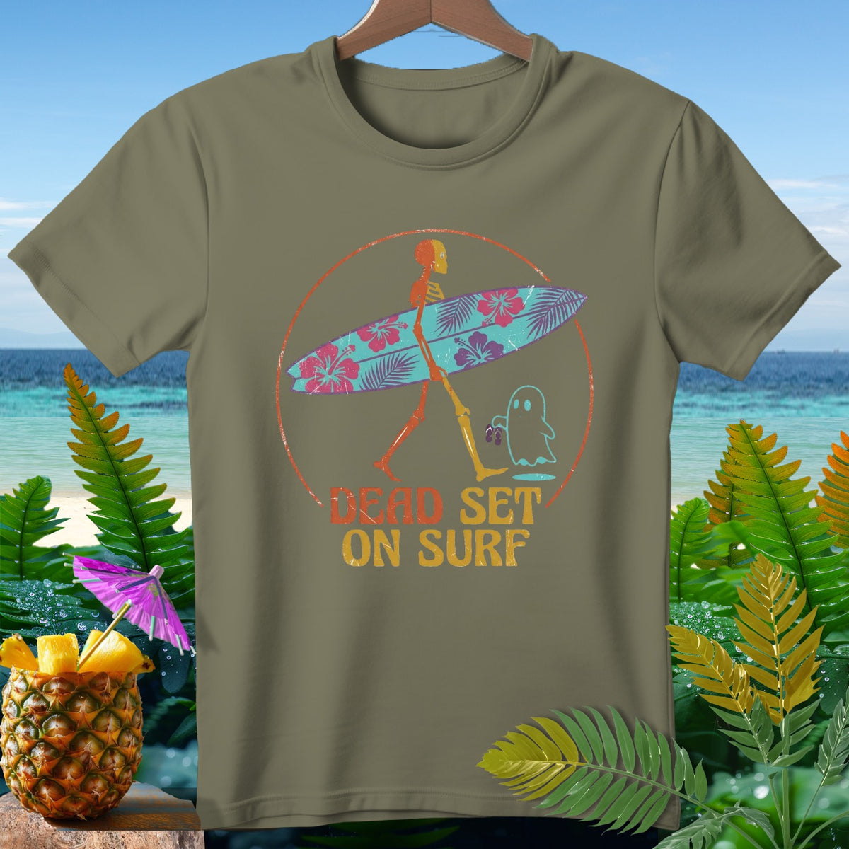 Skeleton with surfboard and ghost, "Dead Set on Surf" text, on olive t-shirt.