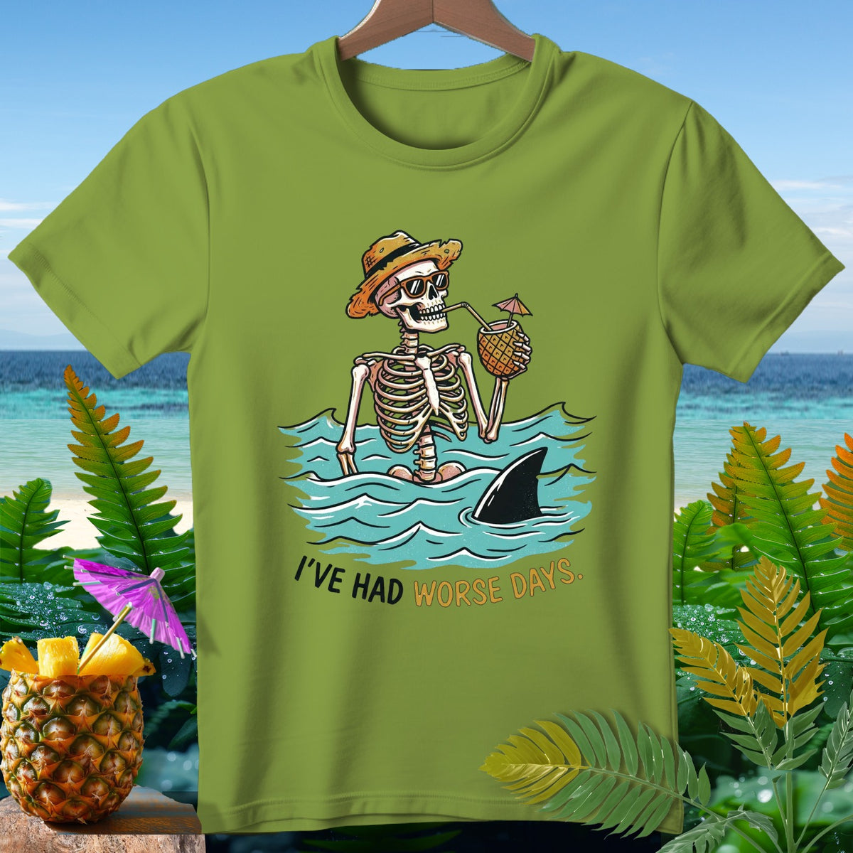 Skeleton in ocean with shark fin and pineapple drink, text "I'VE HAD WORSE DAYS."
