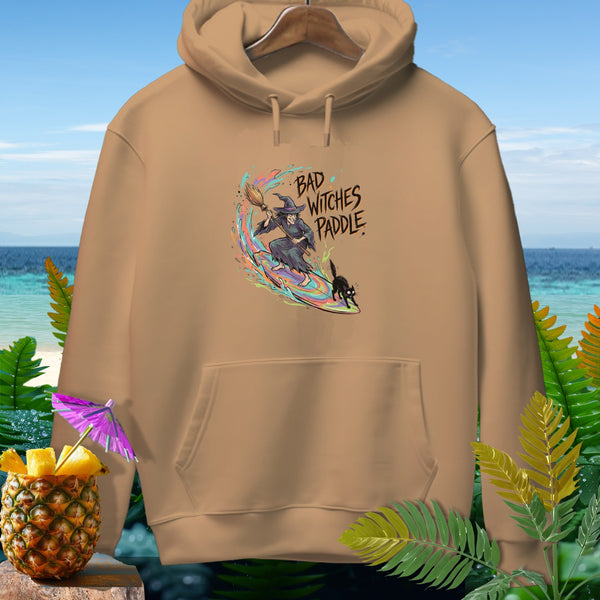 Tan hoodie with graphic of a witch on a surfboard and the text "Bad Witches Paddle".
