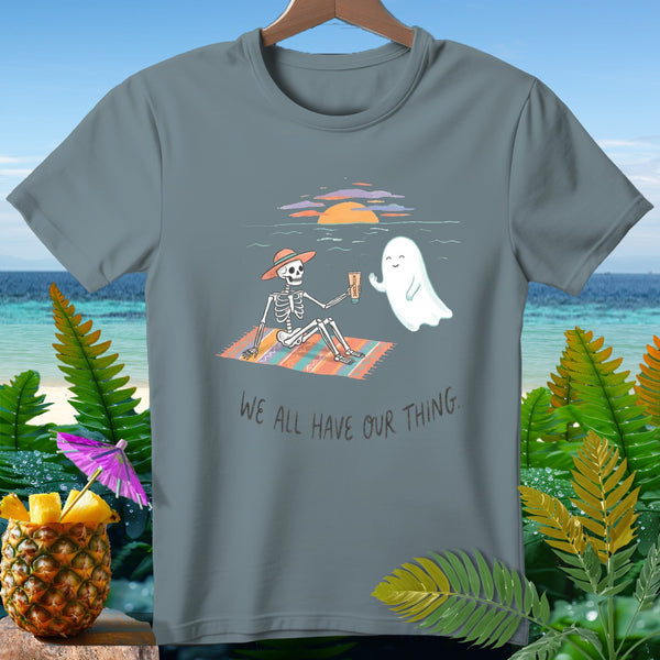 Skeleton and ghost on beach blanket with text "WE ALL HAVE OUR THING."