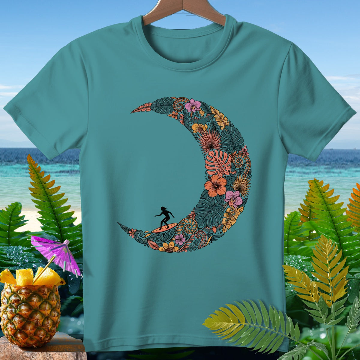 Teal t-shirt with crescent moon design featuring a surfer and tropical floral elements.