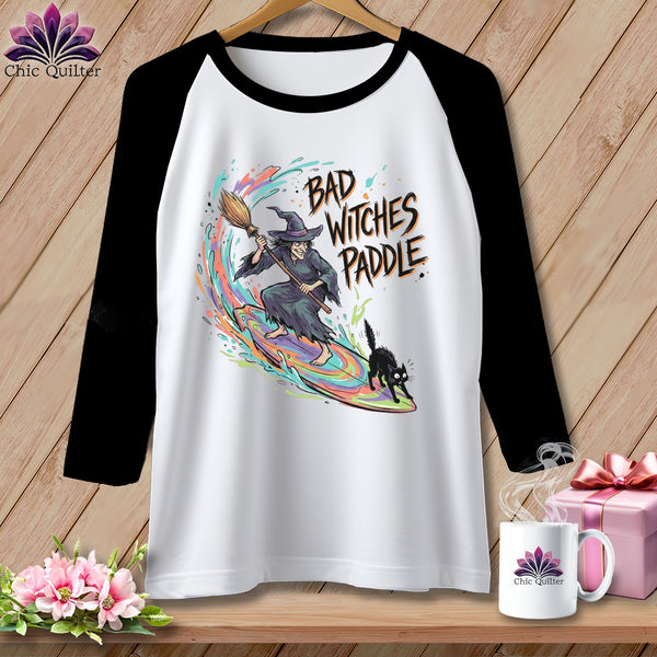 T-shirt with a witch on a surfboard and black cat, text reads "Bad Witches Paddle."