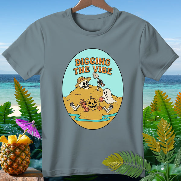 T-shirt graphic with skeleton, ghost, and pumpkin on beach, reads "Digging the Vibe".