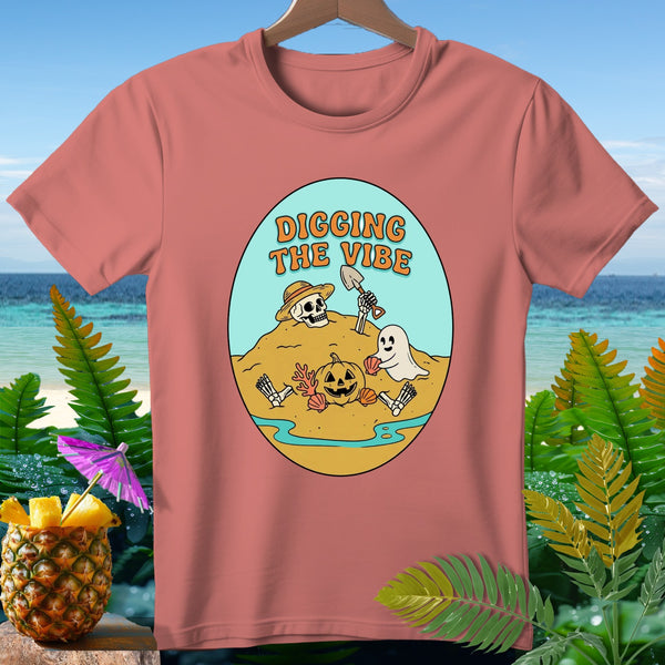 T-shirt with skeleton, ghost, and pumpkin digging on a beach with text "DIGGING THE VIBE".