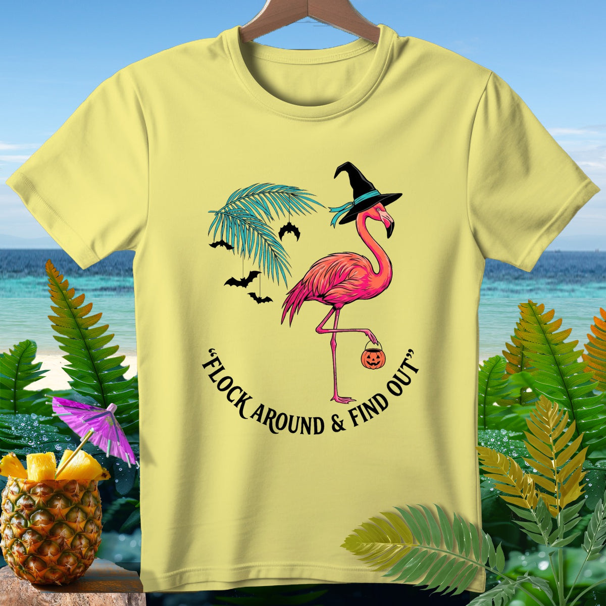 Yellow t-shirt with a flamingo in a witch hat holding a pumpkin, with bats and text.