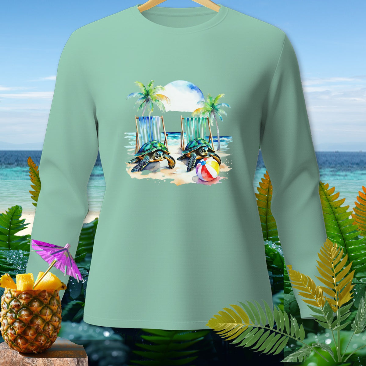 Mint long-sleeve shirt with a watercolor graphic of two turtles on a beach by lounge chairs.