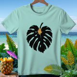 Light blue t-shirt with a black monstera leaf graphic and tropical background.