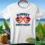White t-shirt with heart-shaped sunglasses reflecting a sunset and palm trees.