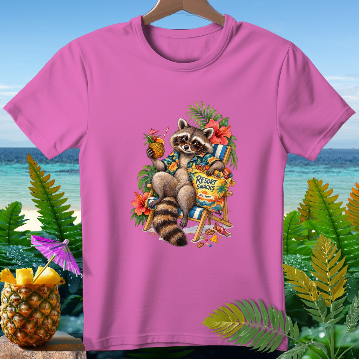 Pink t-shirt with raccoon in lounge chair holding pineapple drink and "Resort Snacks" bag.