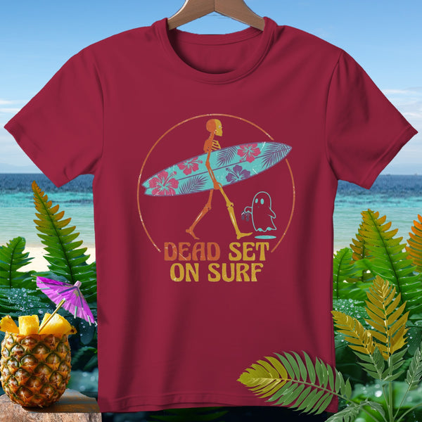 Maroon t-shirt with skeleton carrying surfboard and ghost. Text: "DEAD SET ON SURF".