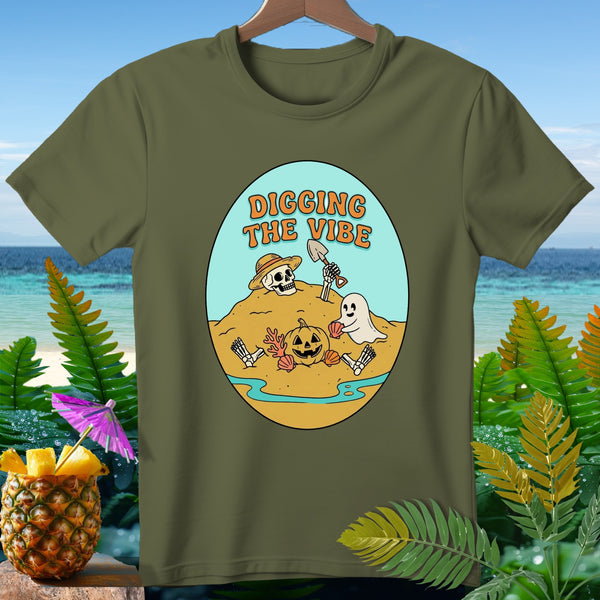 Green t-shirt with cartoon skeleton, ghost, and pumpkin digging on a beach.