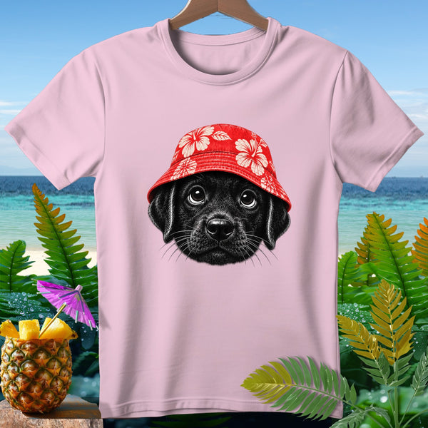 Pink t-shirt with black puppy wearing a red floral bucket hat, tropical background.