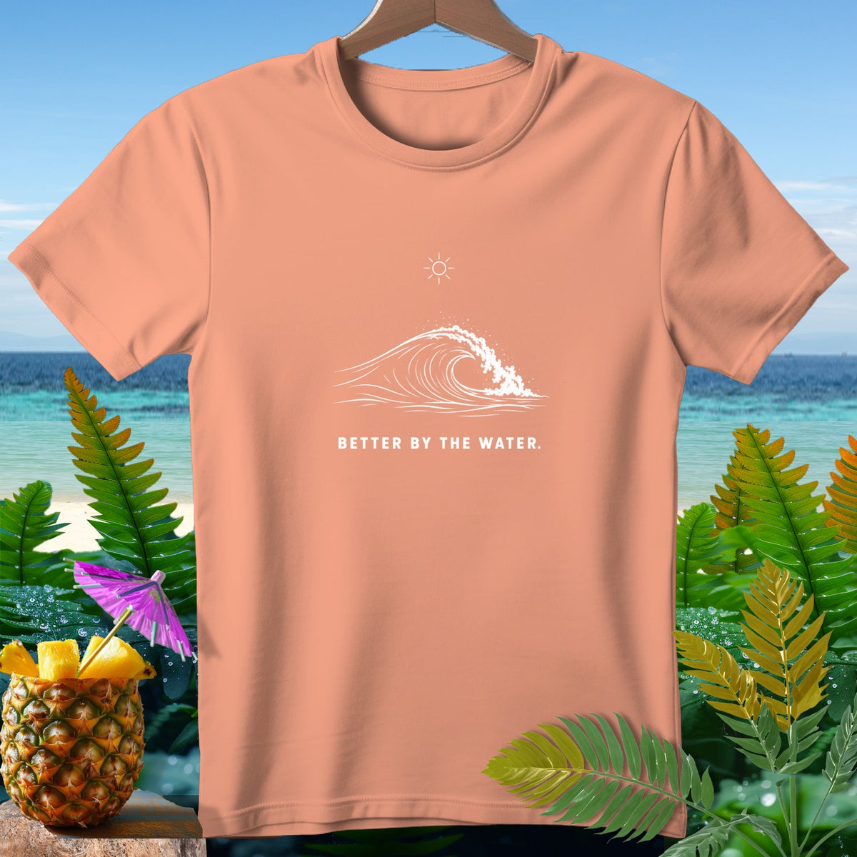Peach t-shirt with white wave graphic and text "BETTER BY THE WATER."