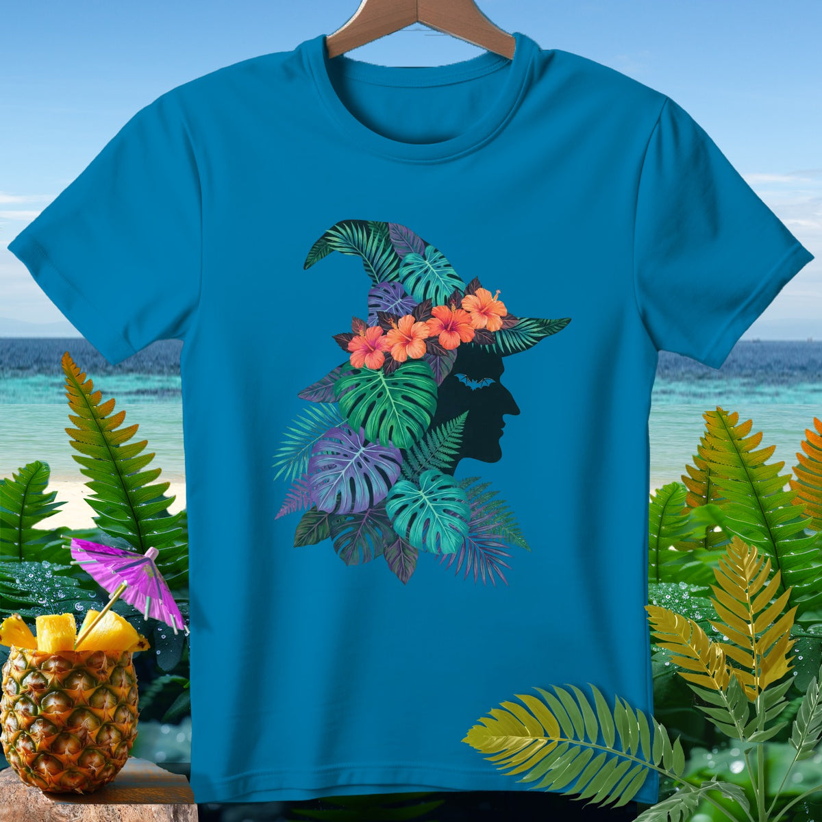 Teal t-shirt with a witch hat design featuring tropical leaves and flowers.