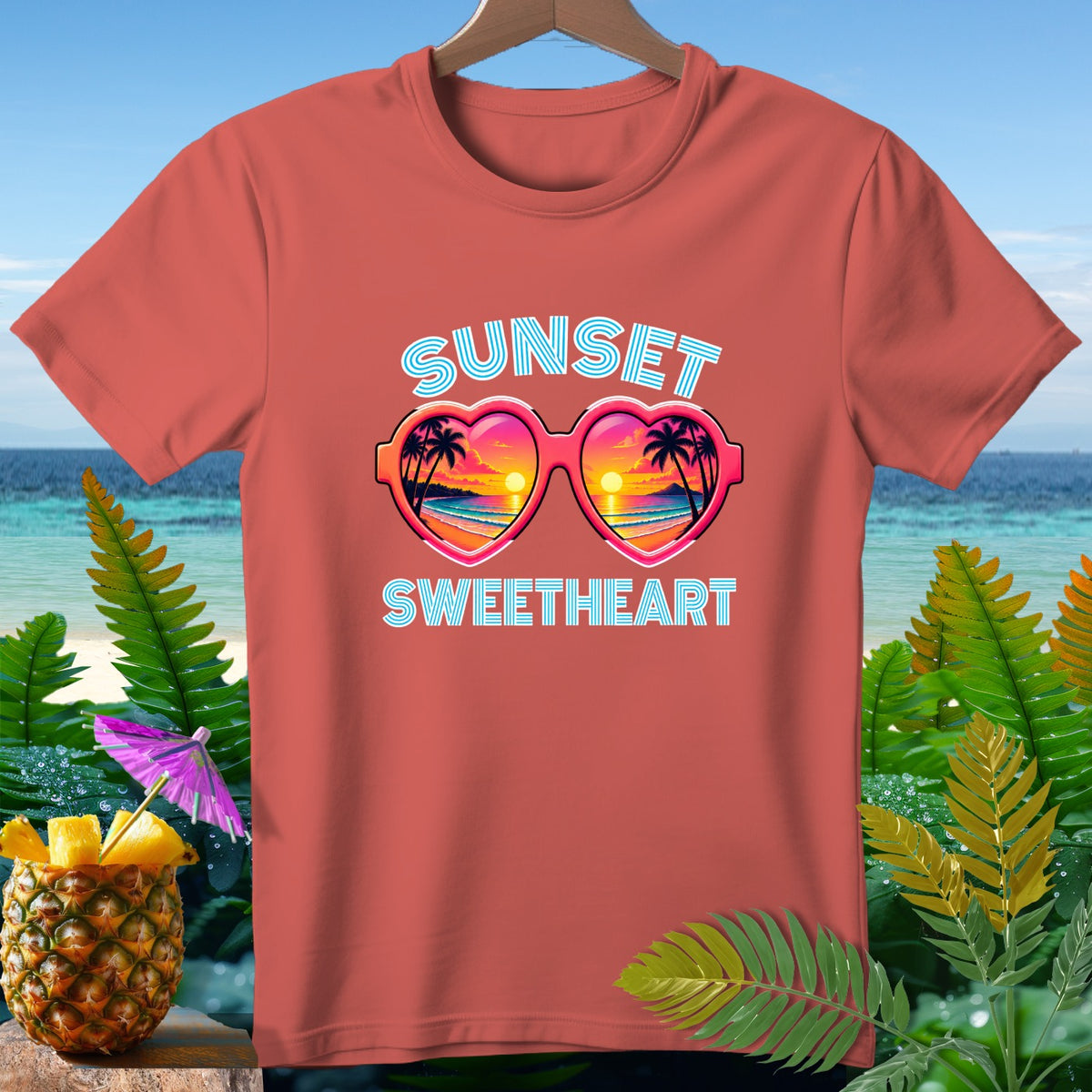 Coral t-shirt with "Sunset Sweetheart" text and heart-shaped sunglasses reflecting a sunset.